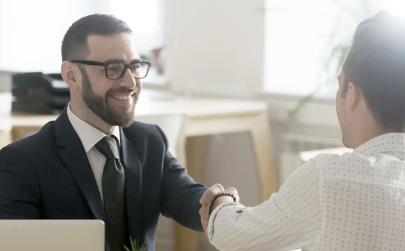un hombre sonriente y elegante dando la mano a otro vestido de forma más informal