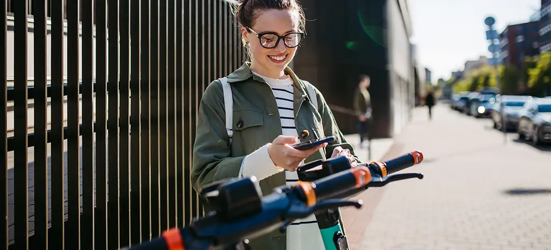 Chica joven colocando el móvil en un patinetes eléctricos para circular