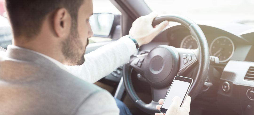 Joven con un mano en el volante y con el móvil en la otra mano