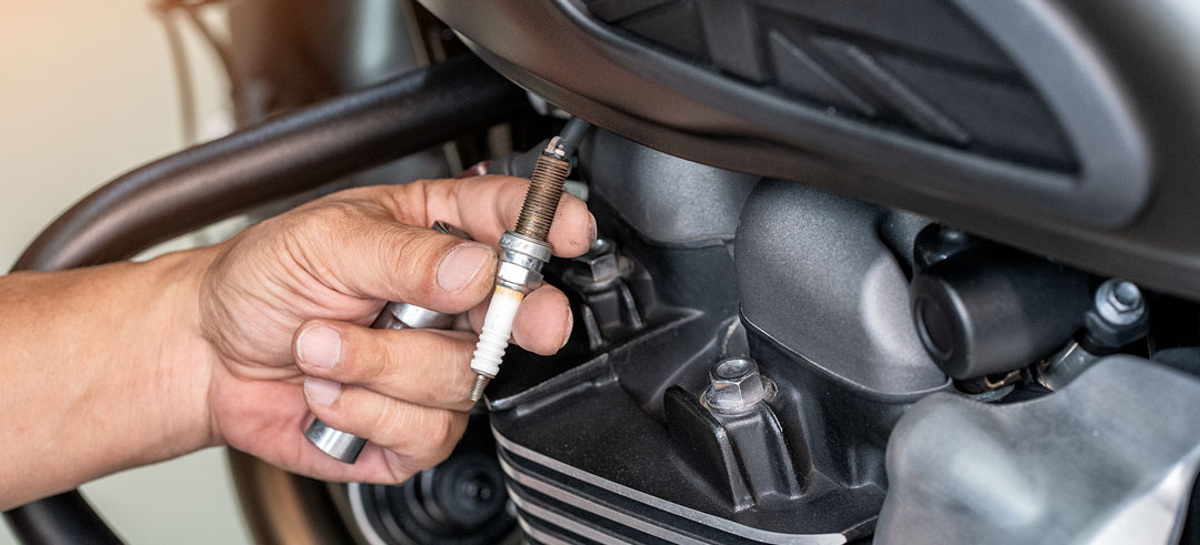 Persona limpiando la bujía de una moto en un taller
